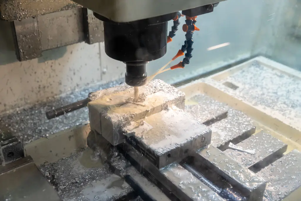 Fräsmaschine bearbeitet ein Aluminiumteil, ein Mitarbeiter greift in den Arbeitsraum